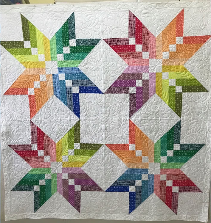 Colorful finished quilt with rainbow star blocks and white quilted background